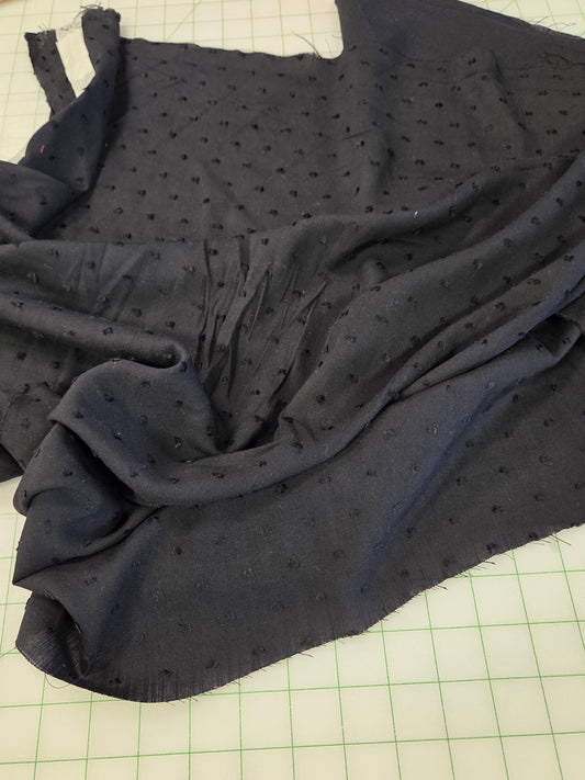 A dark navy blue sheer fabric with a small black dot pattern, draped on a green grid cutting mat with a wooden ruler visible in the top left corner.