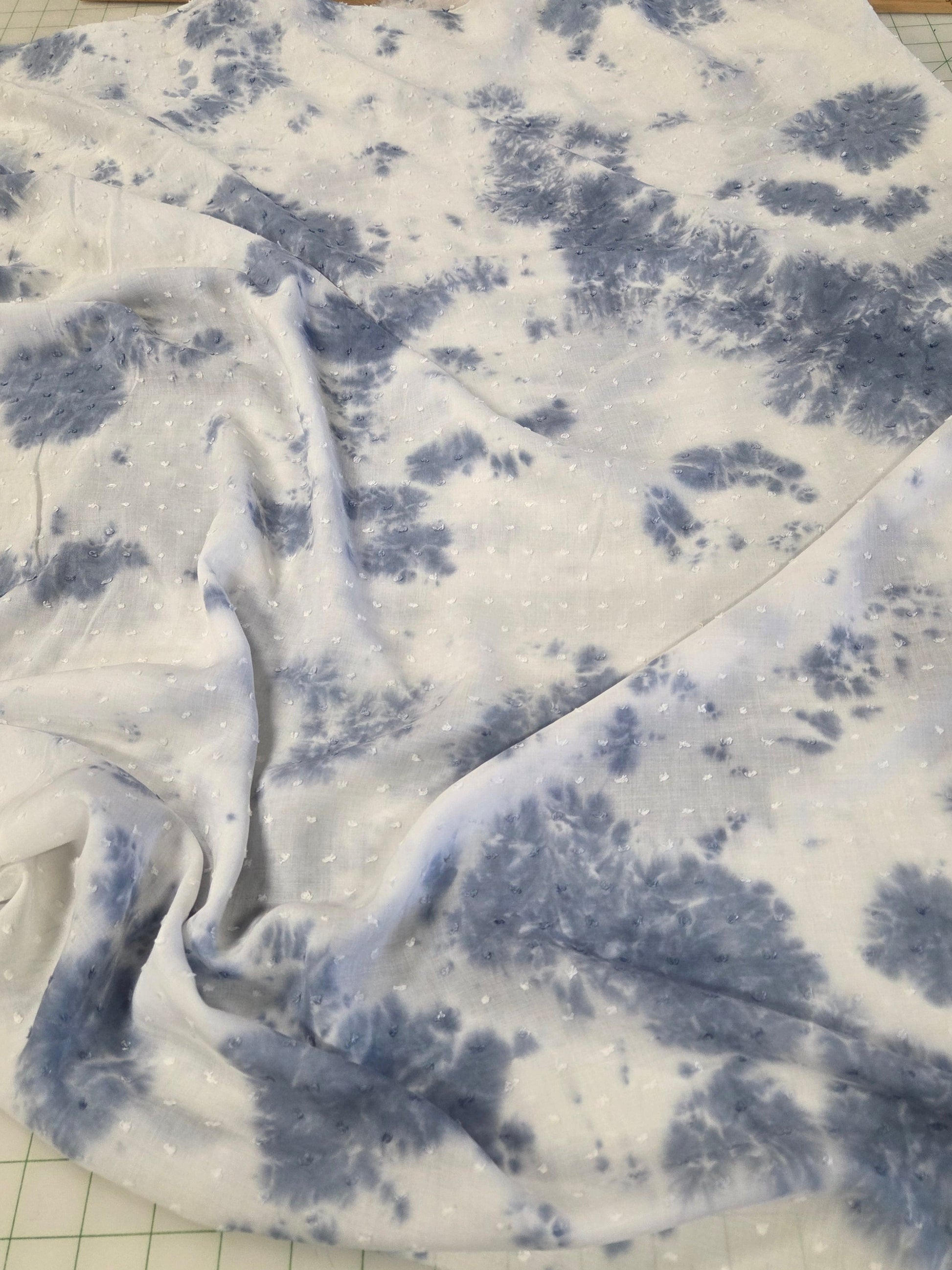 Blue and white tie-dye fabric with a floral pattern, draped over a clear cutting mat with measurement markings.