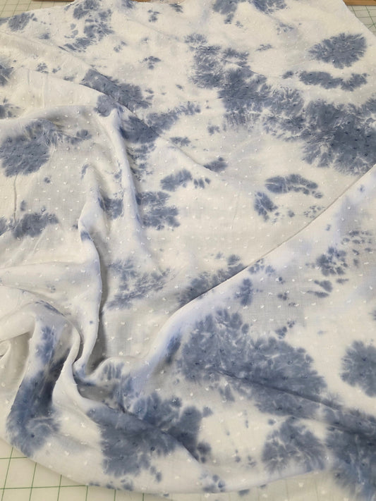 Blue and white tie-dye fabric with a floral pattern, draped over a clear cutting mat with measurement markings.
