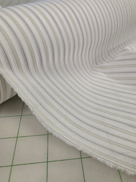A close-up of a white fabric with thin vertical gray stripes, shown draped over a cutting mat in a sewing or fabric store.