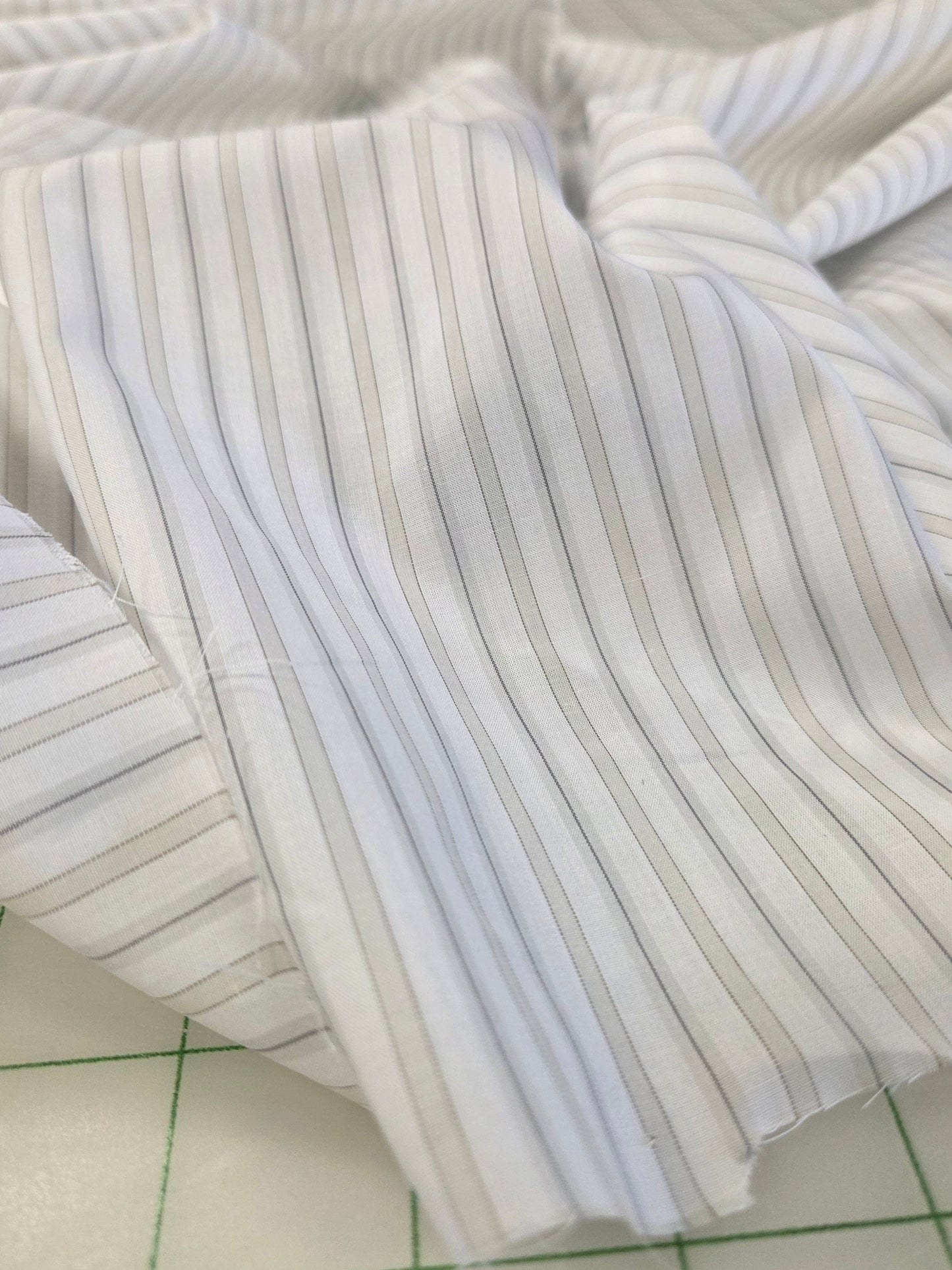 White pinstriped fabric with thin vertical gray stripes, draped on a green-lined cutting mat.