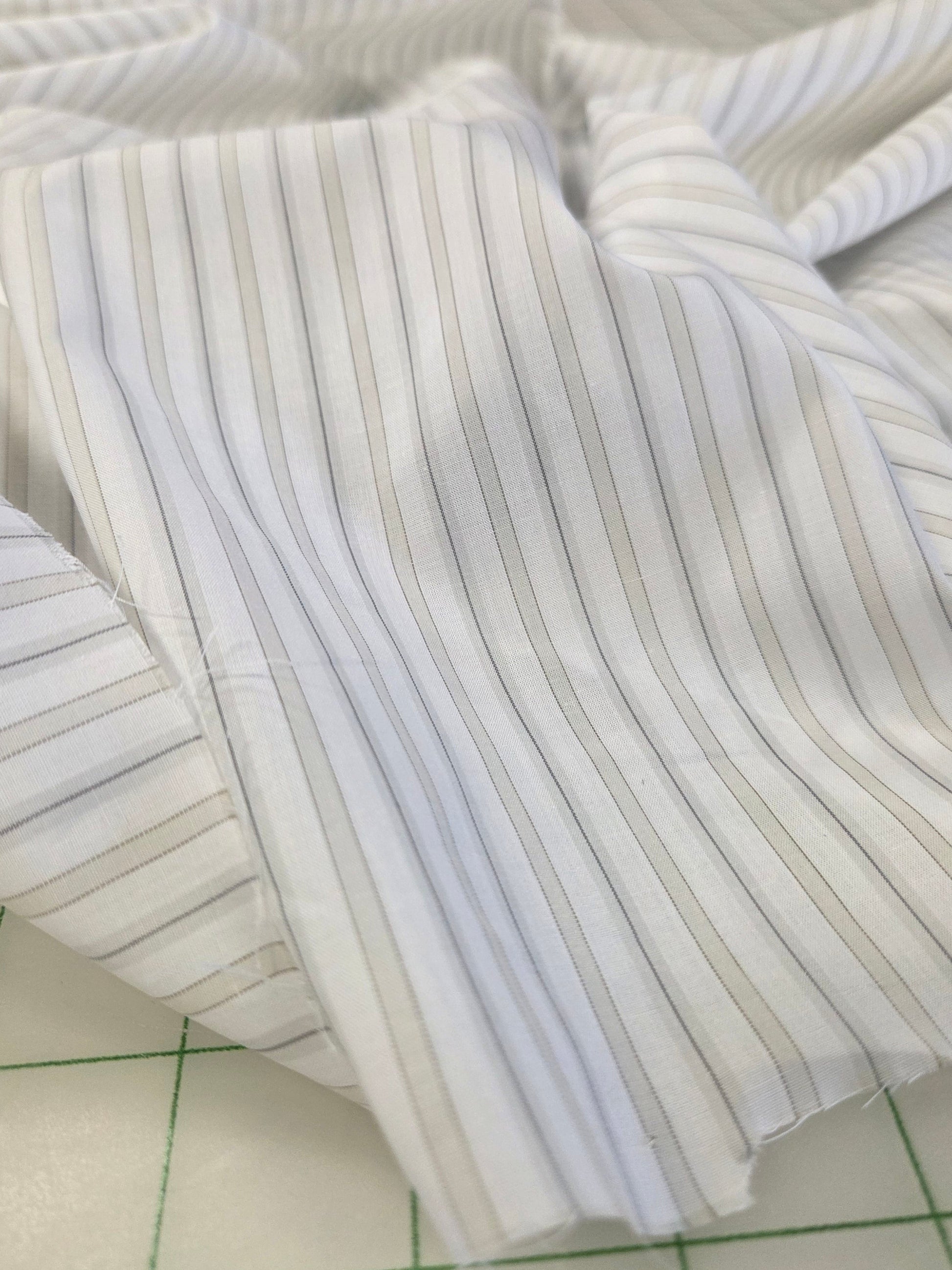 White pinstriped fabric with thin vertical gray stripes, draped on a green-lined cutting mat.