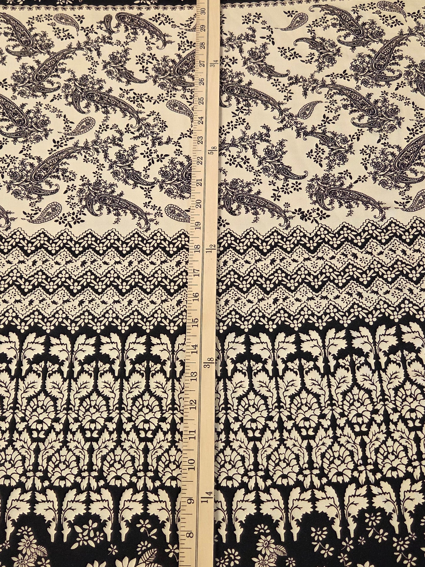 A close-up of a black and cream floral and paisley patterned fabric with a vertical ruler in the center for scale.