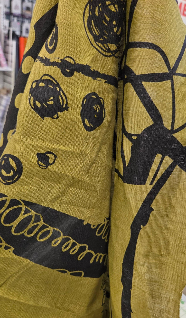 A close-up of a mustard yellow fabric with a black abstract print, draped over a table in a sewing or fabric store.