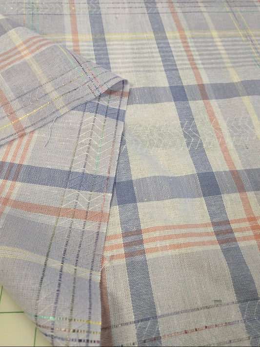 A close-up of plaid fabric with a light blue-gray base, white stripes, and thin orange and yellow lines, folded over to show the texture and stitching.
