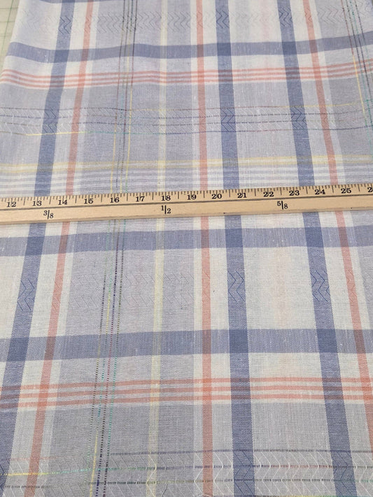 A plaid fabric cloth with blue, white, and orange stripes laid flat on a green cutting mat with a wooden ruler placed across the middle to show dimensions.
