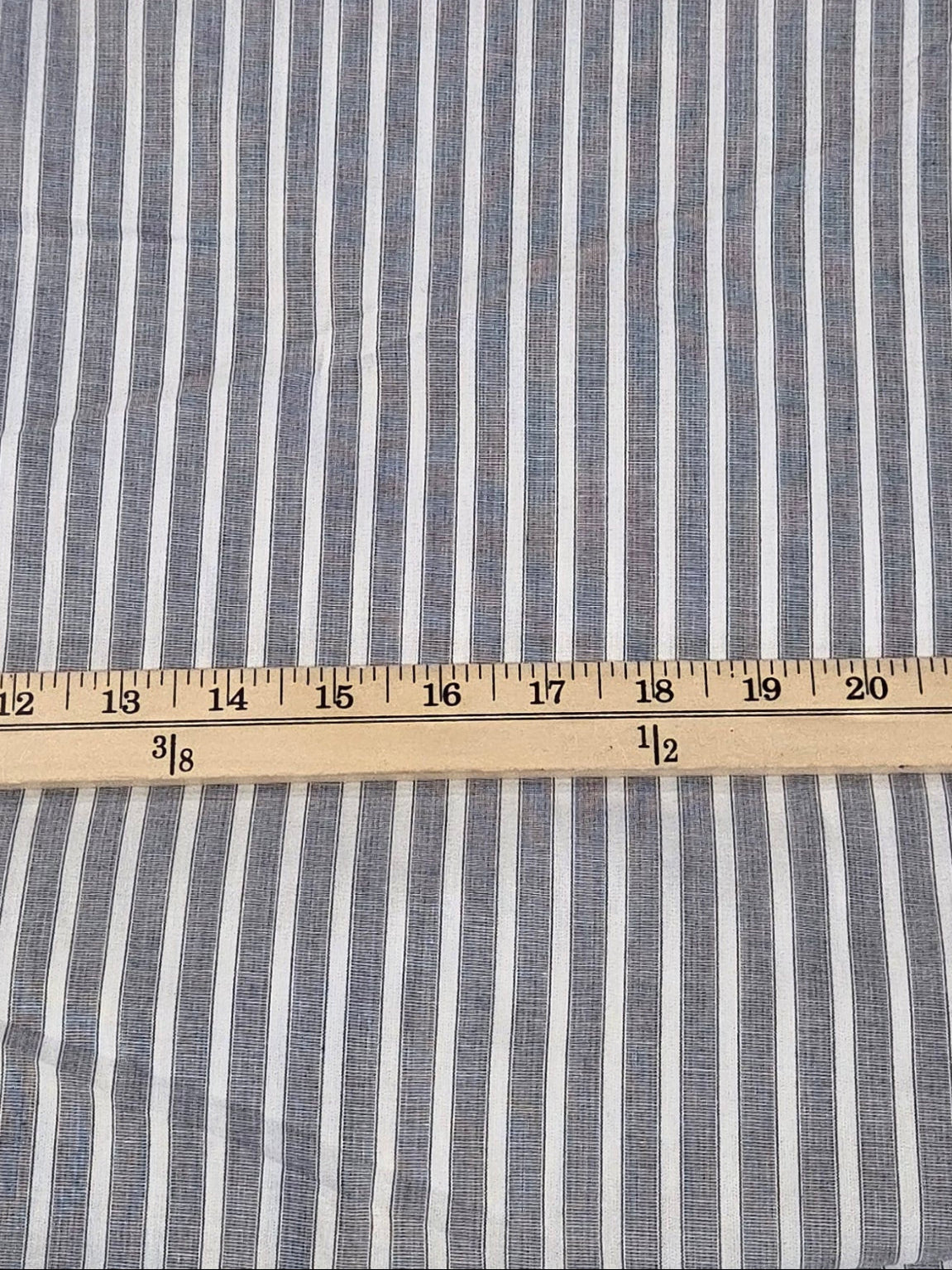 A folded piece of blue and white vertically striped fabric laid flat on a green grid cutting mat, with a wooden ruler placed horizontally across the middle to show the stripe pattern and dimensions.