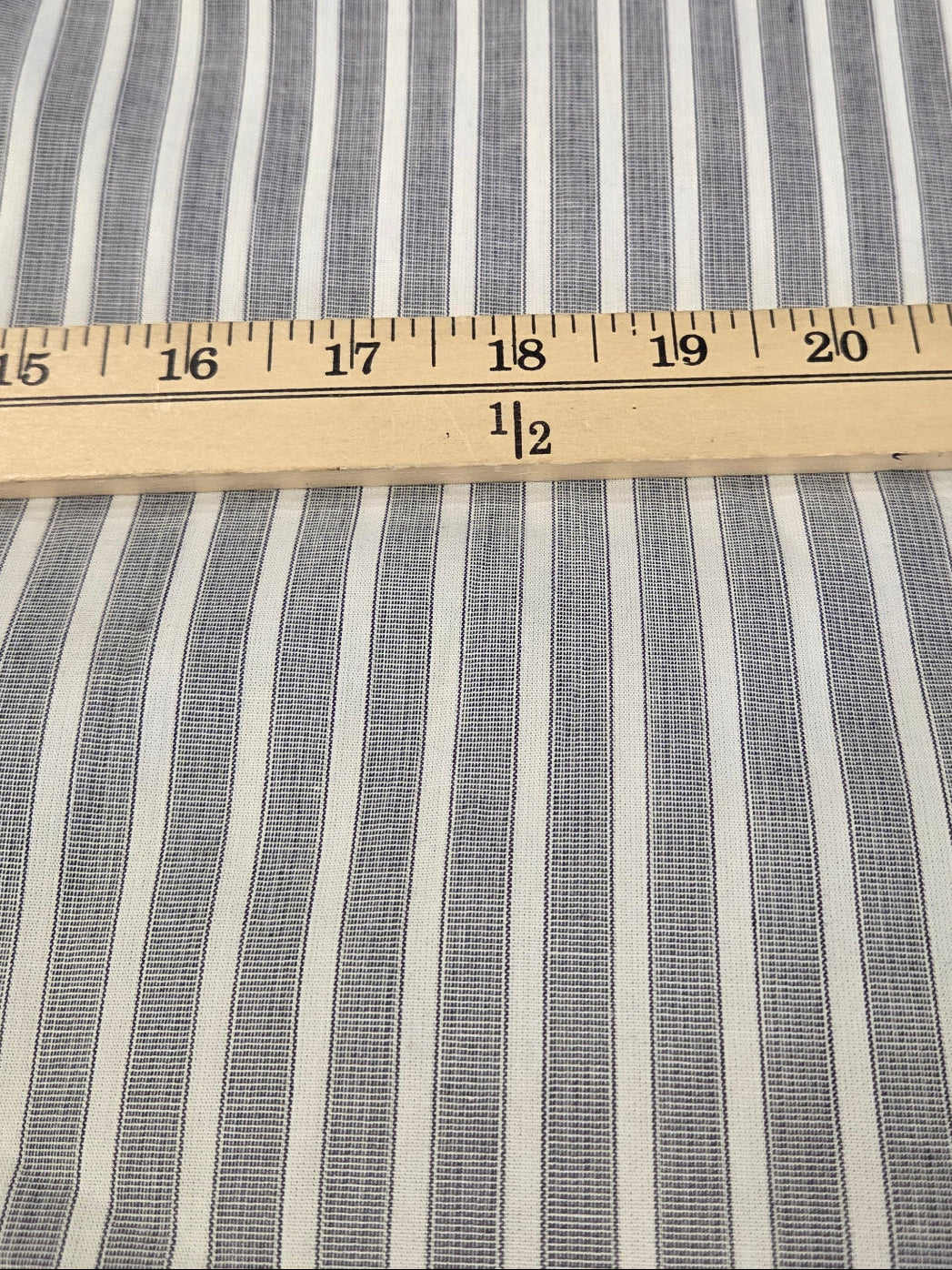 Blue and white vertically striped fabric with a wooden ruler laid horizontally for scale.