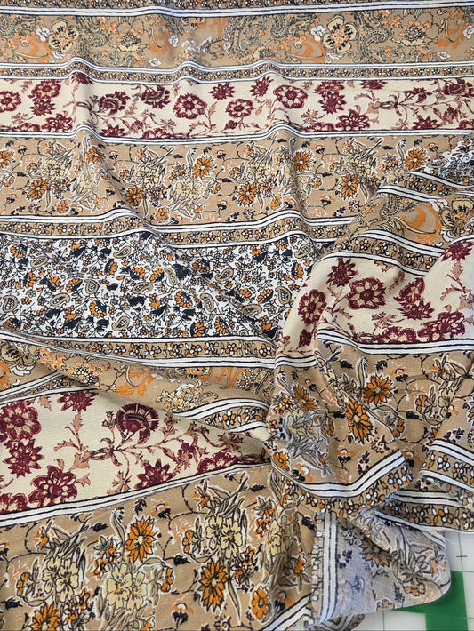 A draped piece of fabric with an intricate, multi-colored floral and ornamental pattern in beige, burgundy, orange, and gray, laid out on a green surface.