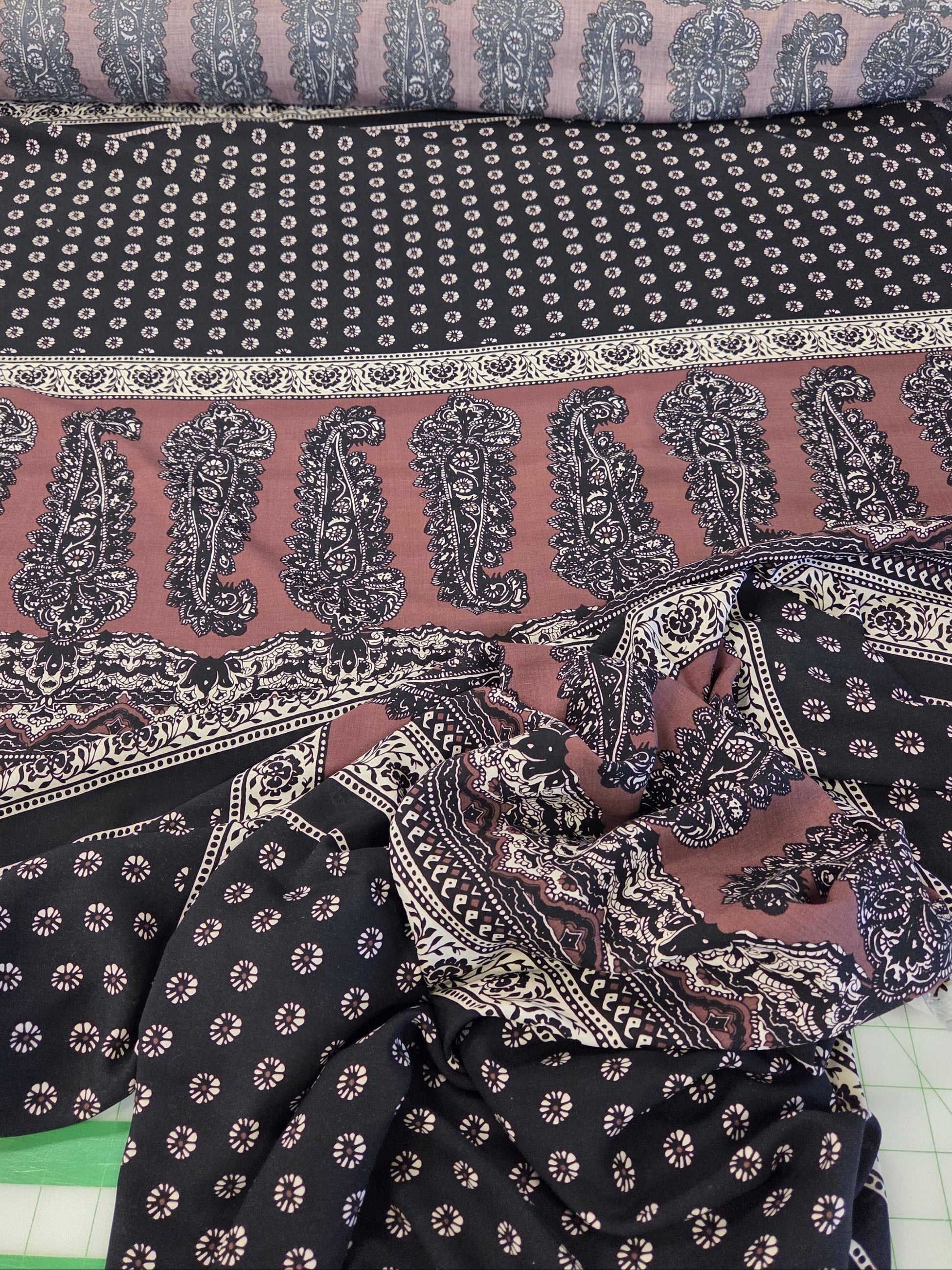 A close-up of patterned fabric laid out on a surface, showing a dark navy base with small white floral motifs, a dusty rose border with large navy paisley prints, and a matching rolled section at the top.