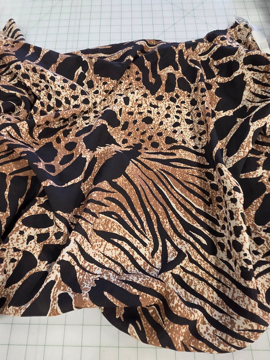 A leopard print fabric with a mix of black, brown, and beige animal spots and stripes, draped on a white gridded cutting mat in a sewing or tailoring room.