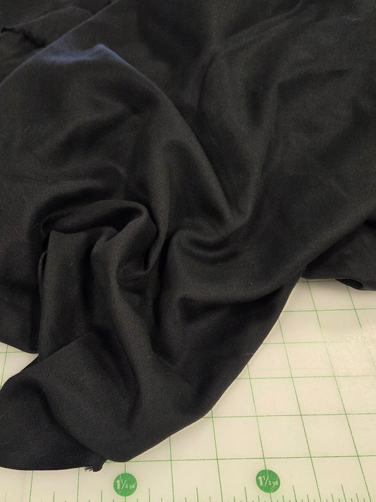 A draped piece of black fabric with a smooth, slightly shiny texture, laid out on a white cutting mat with green grid lines and measurements.
