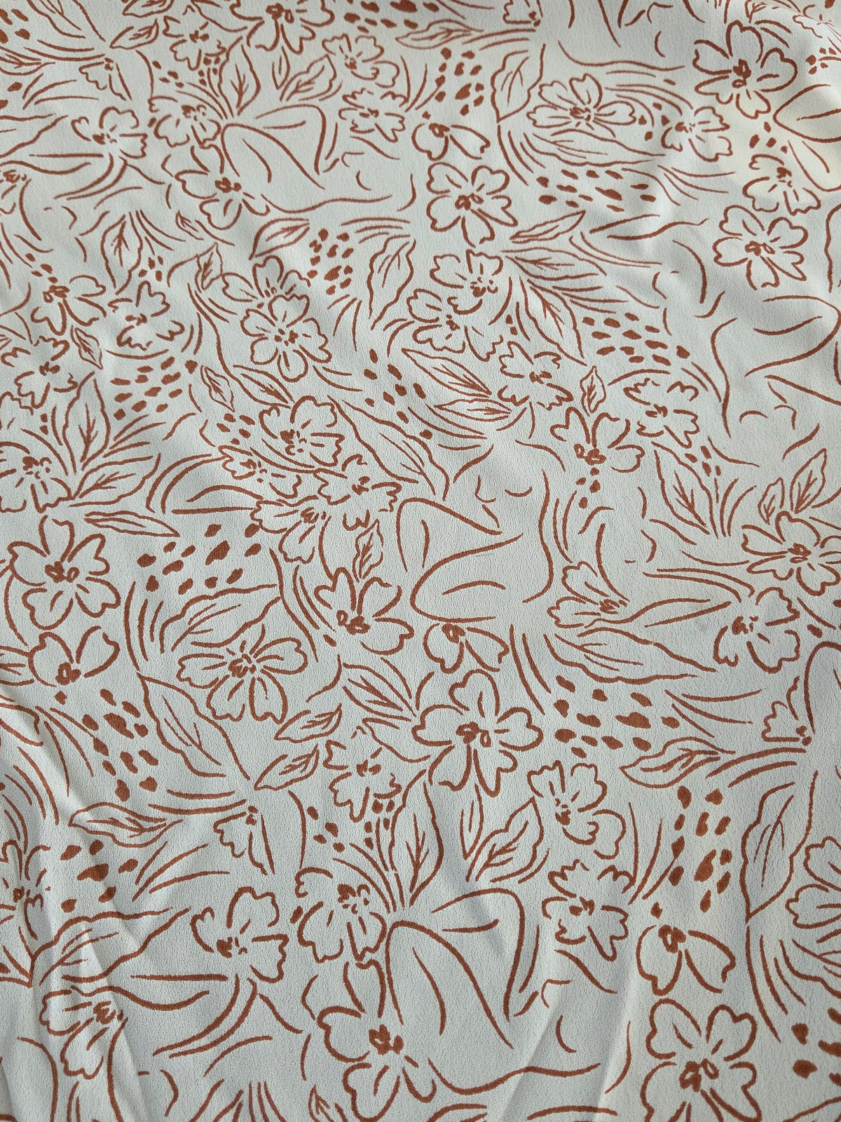 A close-up of a light beige or off-white fabric with an all-over brown floral line pattern.