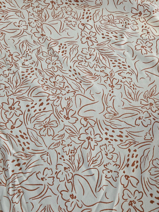 A close-up of a light beige or off-white fabric with an all-over brown floral line pattern.