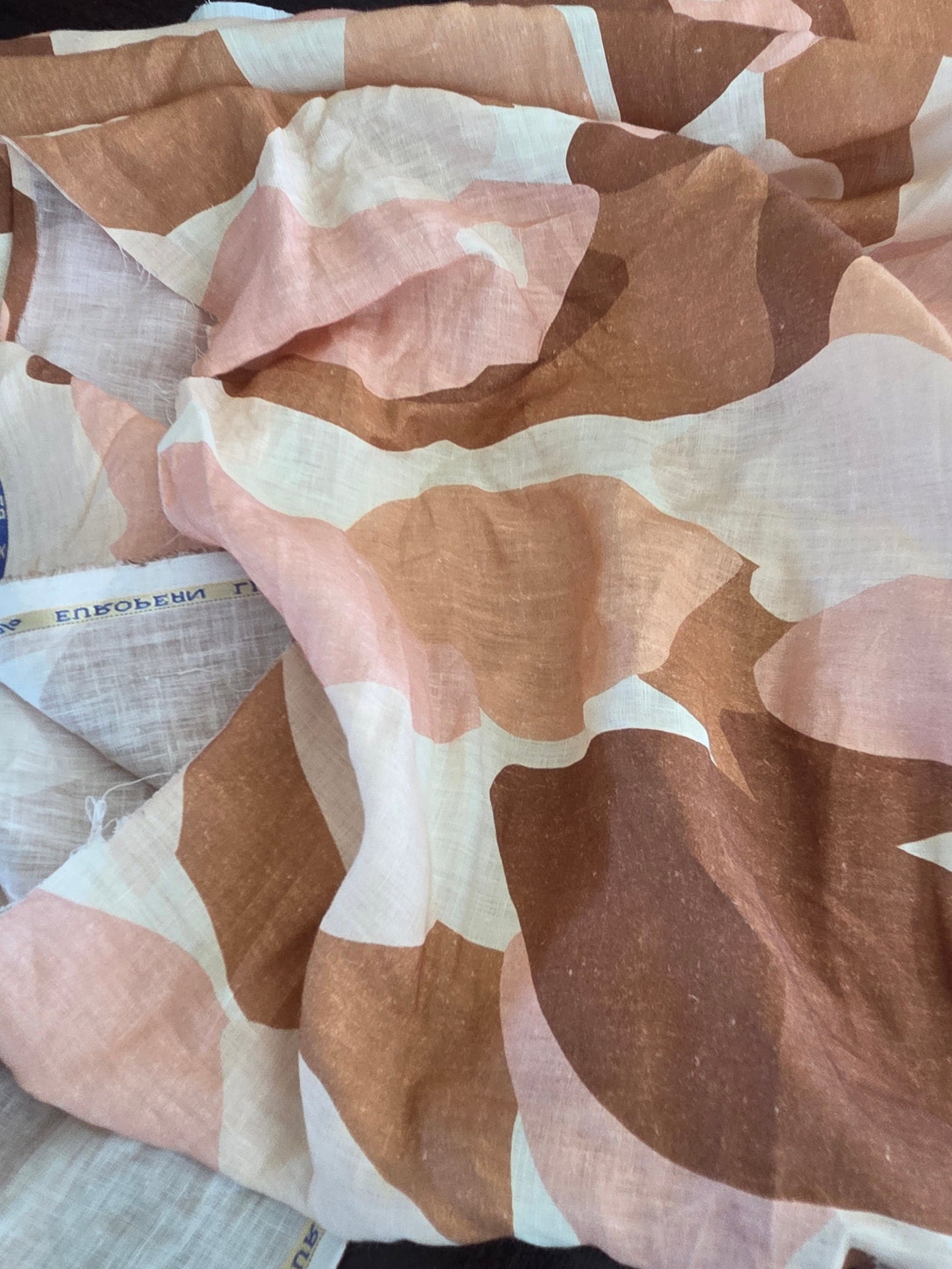 A close-up of a lightweight fabric with an abstract organic pattern in shades of brown, dusty pink, and off-white, draped on a dark surface.