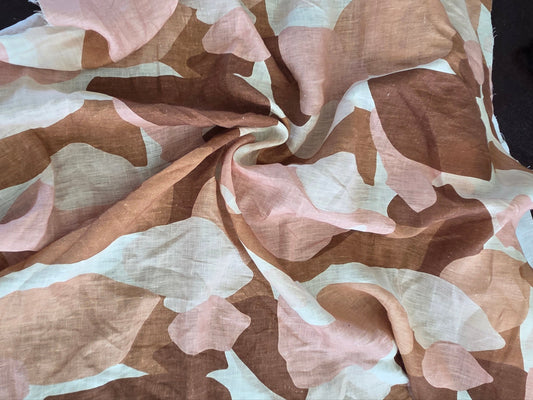 A draped piece of lightweight fabric with a soft camouflage pattern in dusty pink, tan, brown, and off-white, laid out on a dark surface.