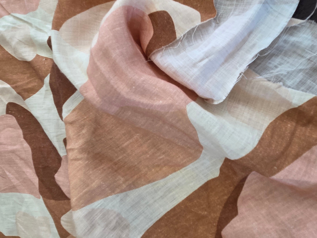 A close-up of draped fabric with an abstract organic pattern in dusty pink, warm brown, cream, and off-white.