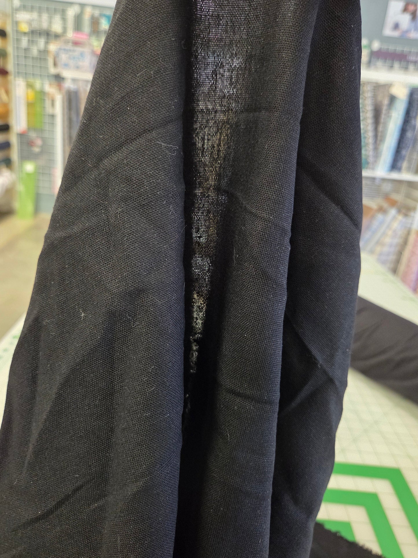 A close-up of a black linen fabric being held up in a sewing or fabric store, showing its texture and weave.