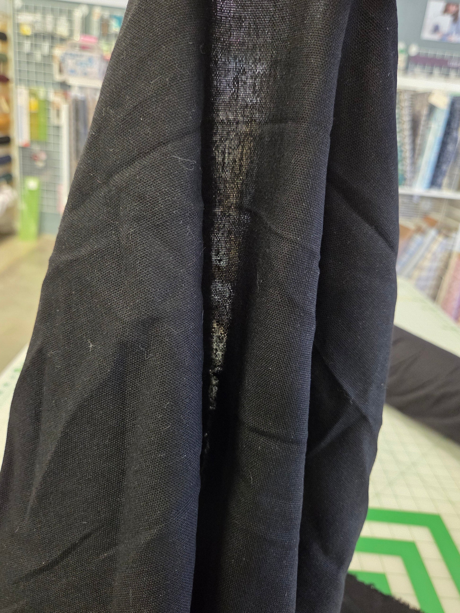 A close-up of a black linen fabric being held up in a sewing or fabric store, showing its texture and weave.