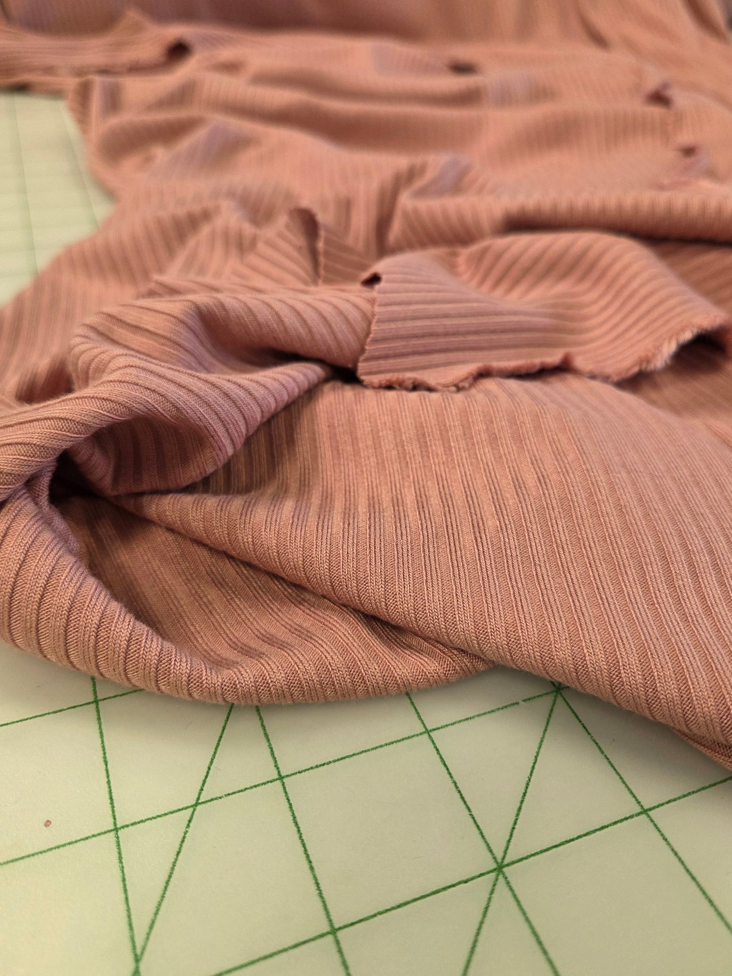 A close-up of a dusty rose ribbed knit fabric draped over a green cutting mat.