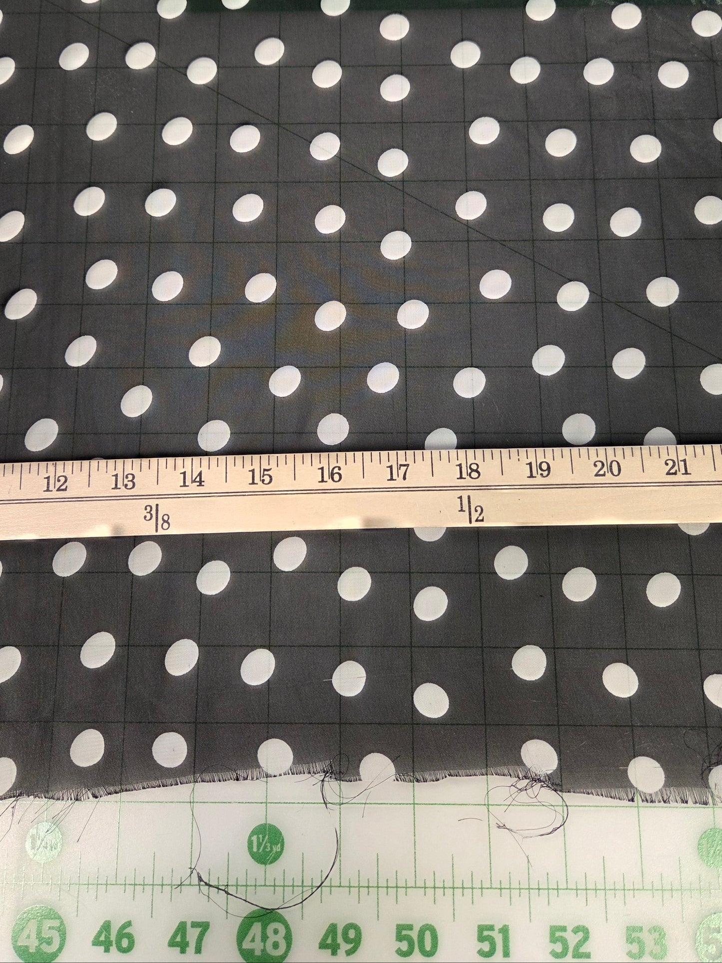 Black fabric with a white polka dot pattern, shown with a wooden ruler and a green measuring tape to indicate scale.