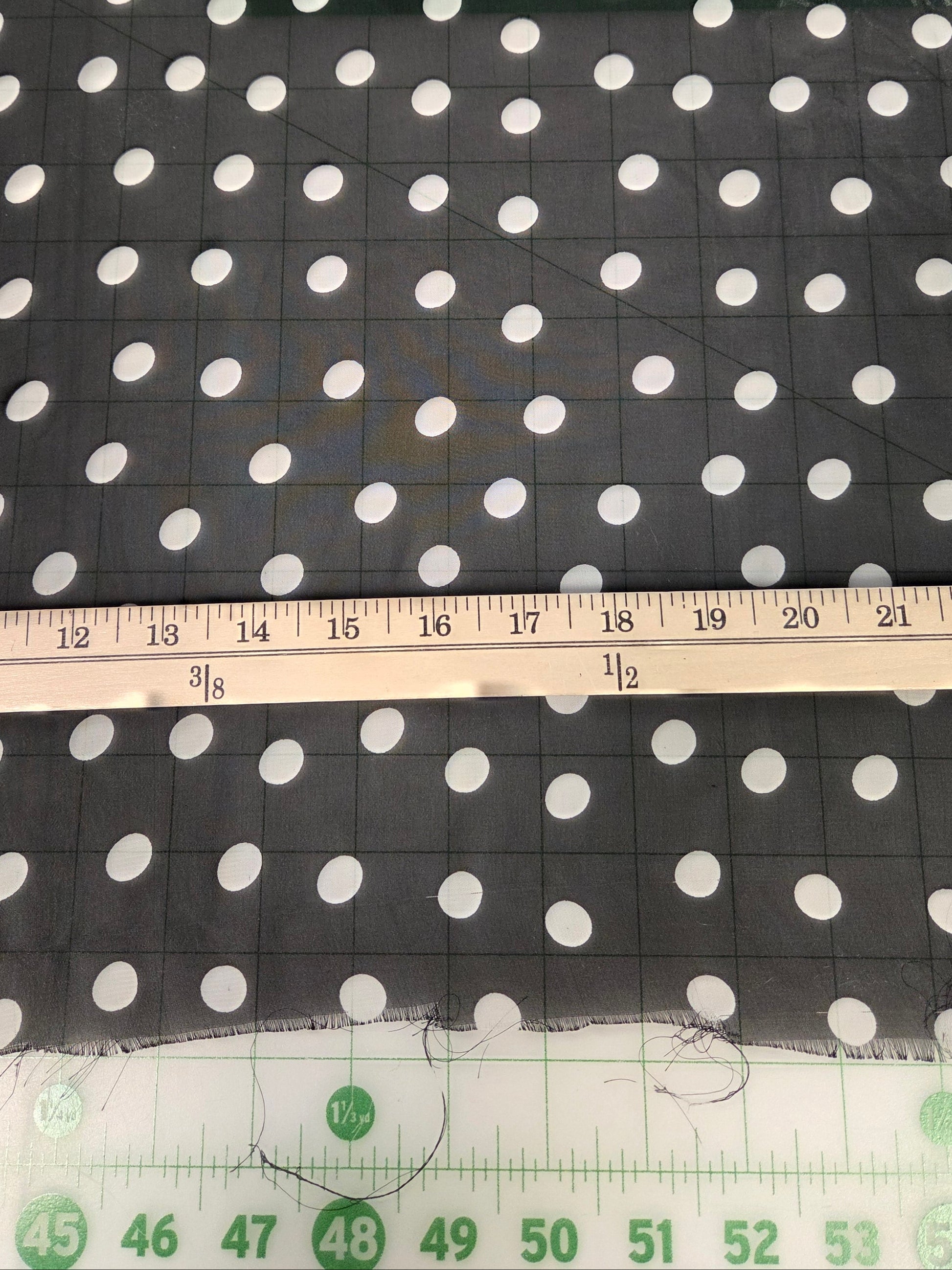 Black fabric with a white polka dot pattern, shown with a wooden ruler and a green measuring tape to indicate scale.