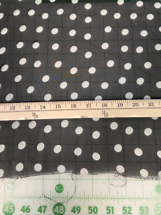 Black fabric with a white polka dot pattern, shown with a wooden ruler and a green measuring tape to indicate scale.