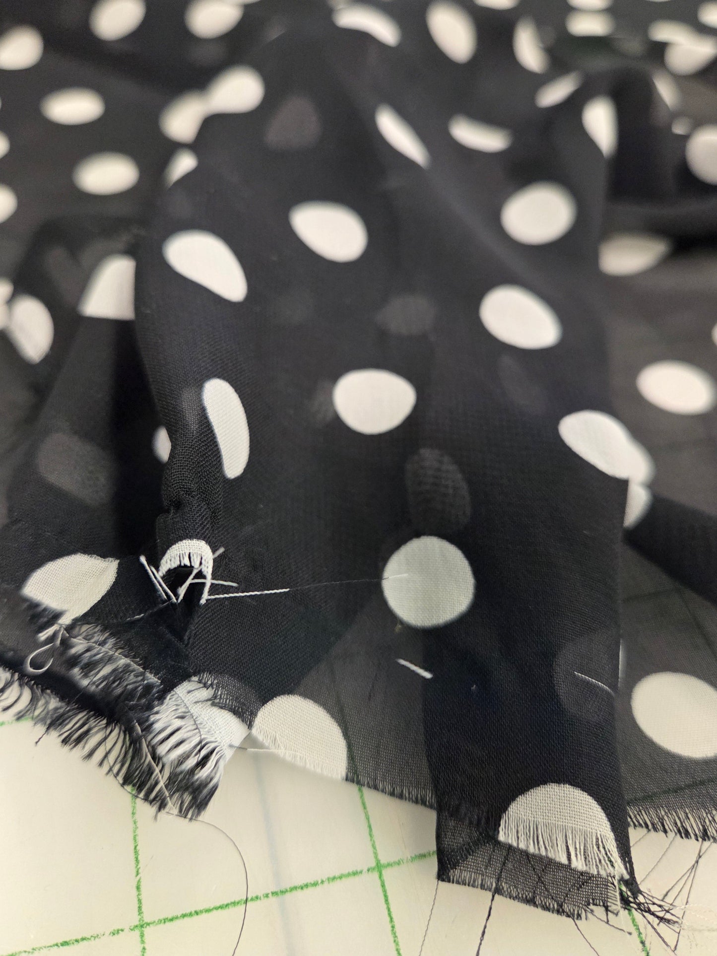 Black sheer mesh fabric with large white polka dots and frayed edges, draped over a white cutting mat with grid lines.