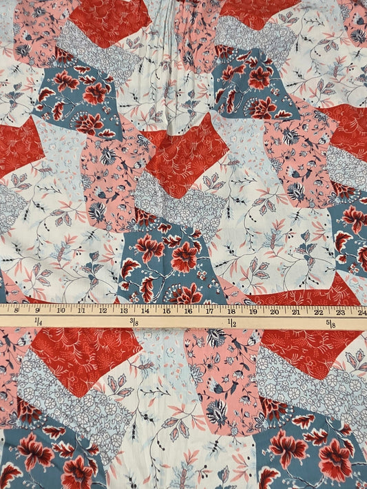 A patchwork quilted fabric top with a half-zip neckline, laid flat on a cutting mat with a wooden measuring tape ruler across the chest to show scale.