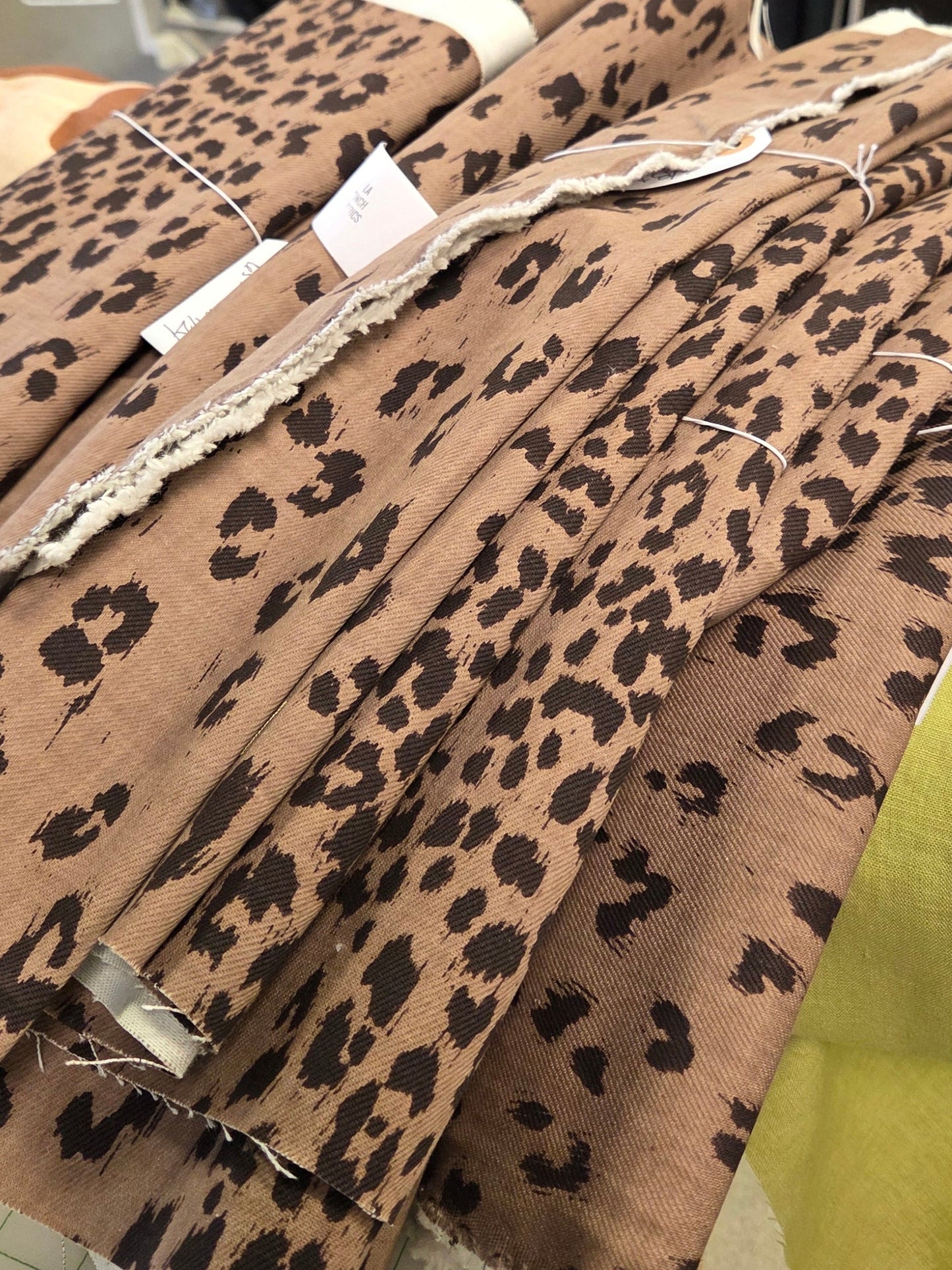 A stack of leopard print fabric bolts in a brown and black pattern, displayed on a table inside a fabric store.