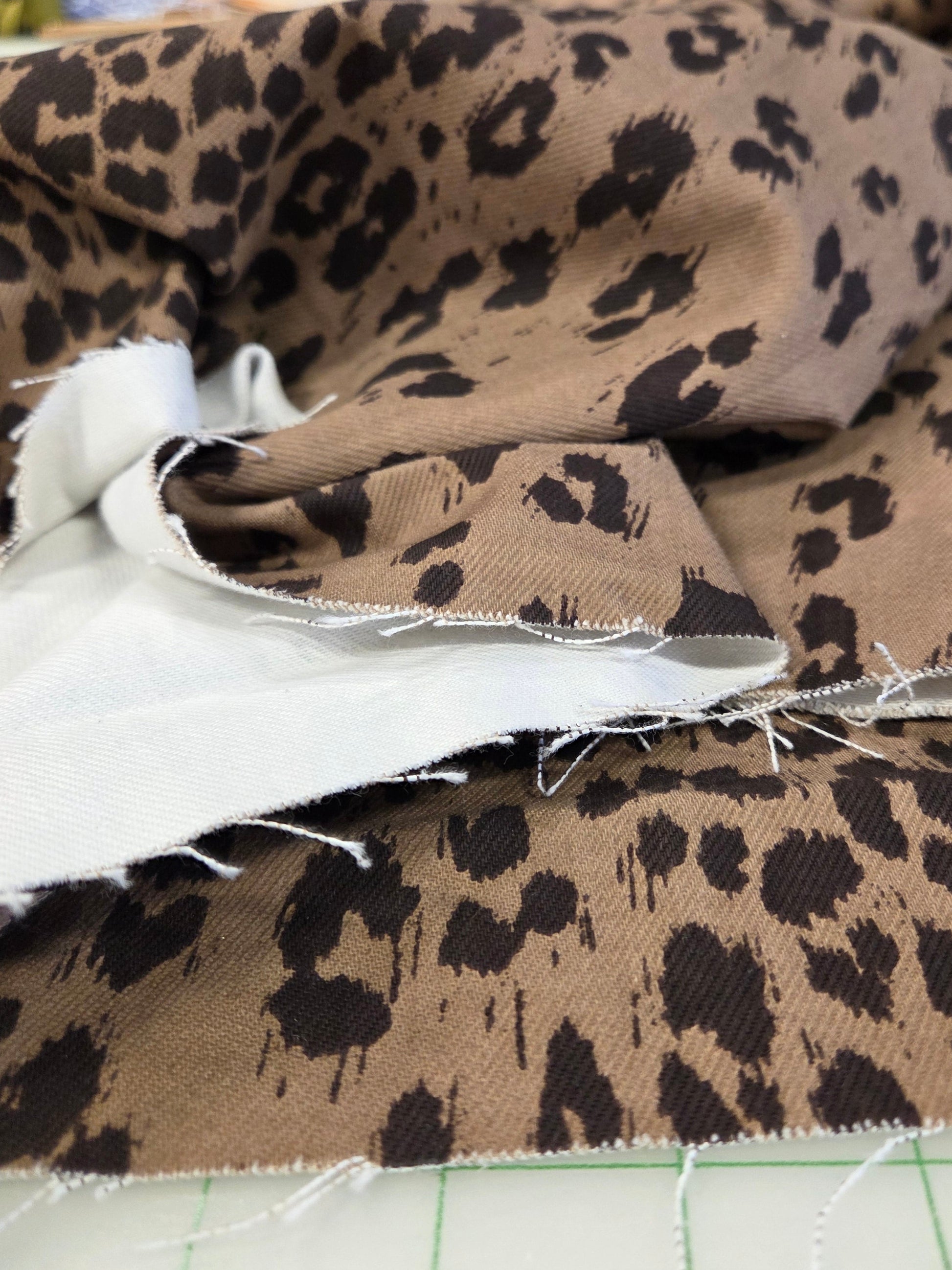 Leopard print fabric in brown and black, folded on a white cutting mat with a white backing visible, in a craft or sewing store setting.