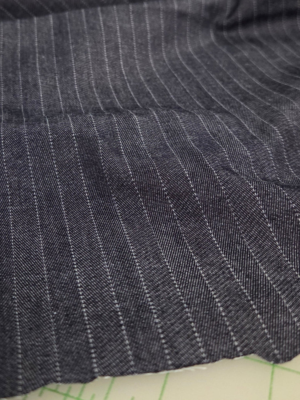 A close-up of dark gray pinstriped fabric with a frayed edge, partially unrolled from a matching fabric roll on a cutting mat inside a sewing or fabric store.