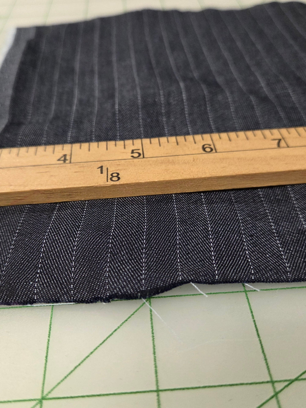 A close-up of a dark navy blue pinstriped fabric measuring approximately 12x18 inches, shown on a green cutting mat with a wooden ruler for scale.
