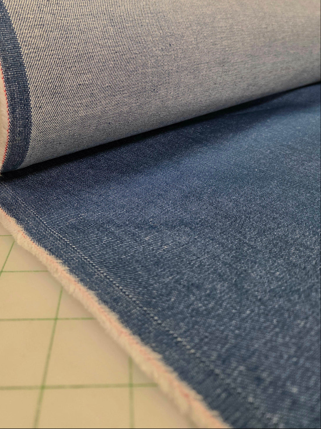A roll of blue-gray woven fabric partially unrolled on a cutting mat inside a craft or sewing studio.