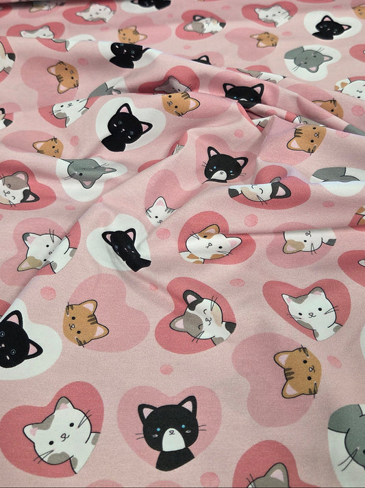 Pink fabric with a repeating pattern of cute cartoon cats inside pink hearts, shown draped with a second folded layer visible at the top.