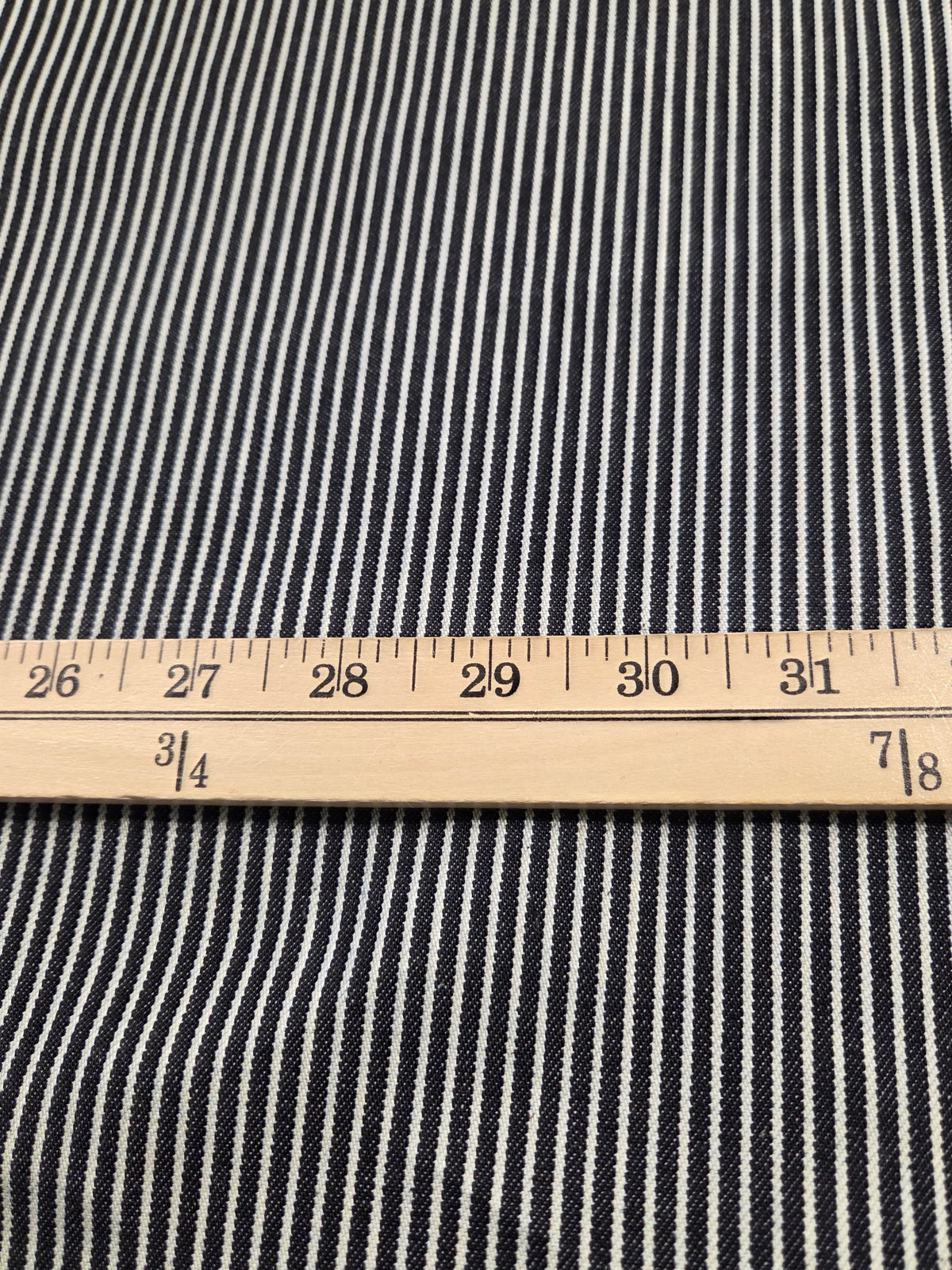 Close-up of a black and white striped fabric with a wooden ruler laid horizontally to show the scale of the pattern.