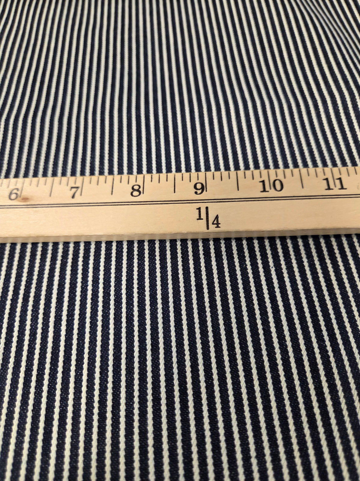 Close-up of a navy and white striped fabric with a wooden ruler placed horizontally to show the pattern scale.