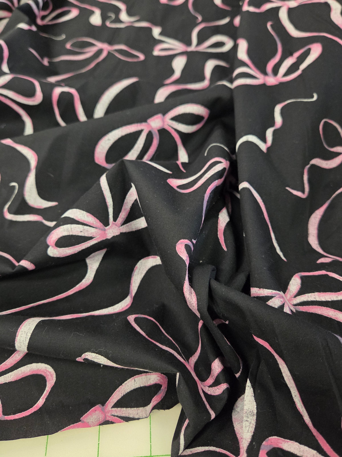 Black fabric with a repeating pink and white bow pattern, draped to show its texture and print. LA Finch Fabrics