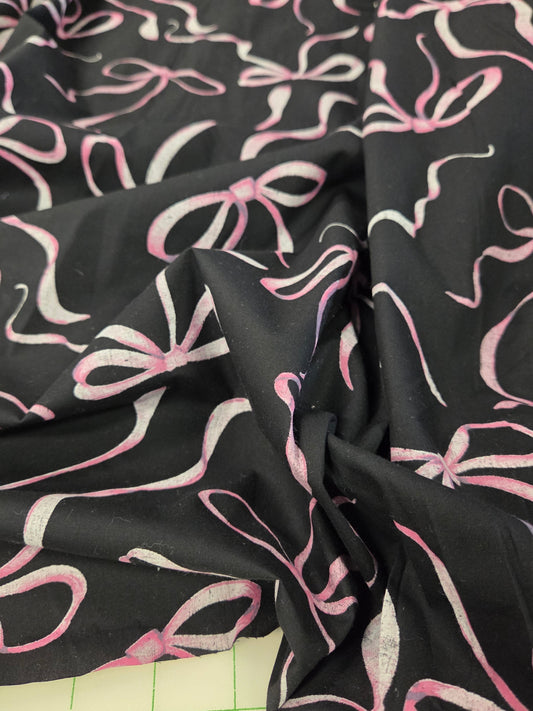 Black fabric with a repeating pink and white bow pattern, draped to show its texture and print. LA Finch Fabrics