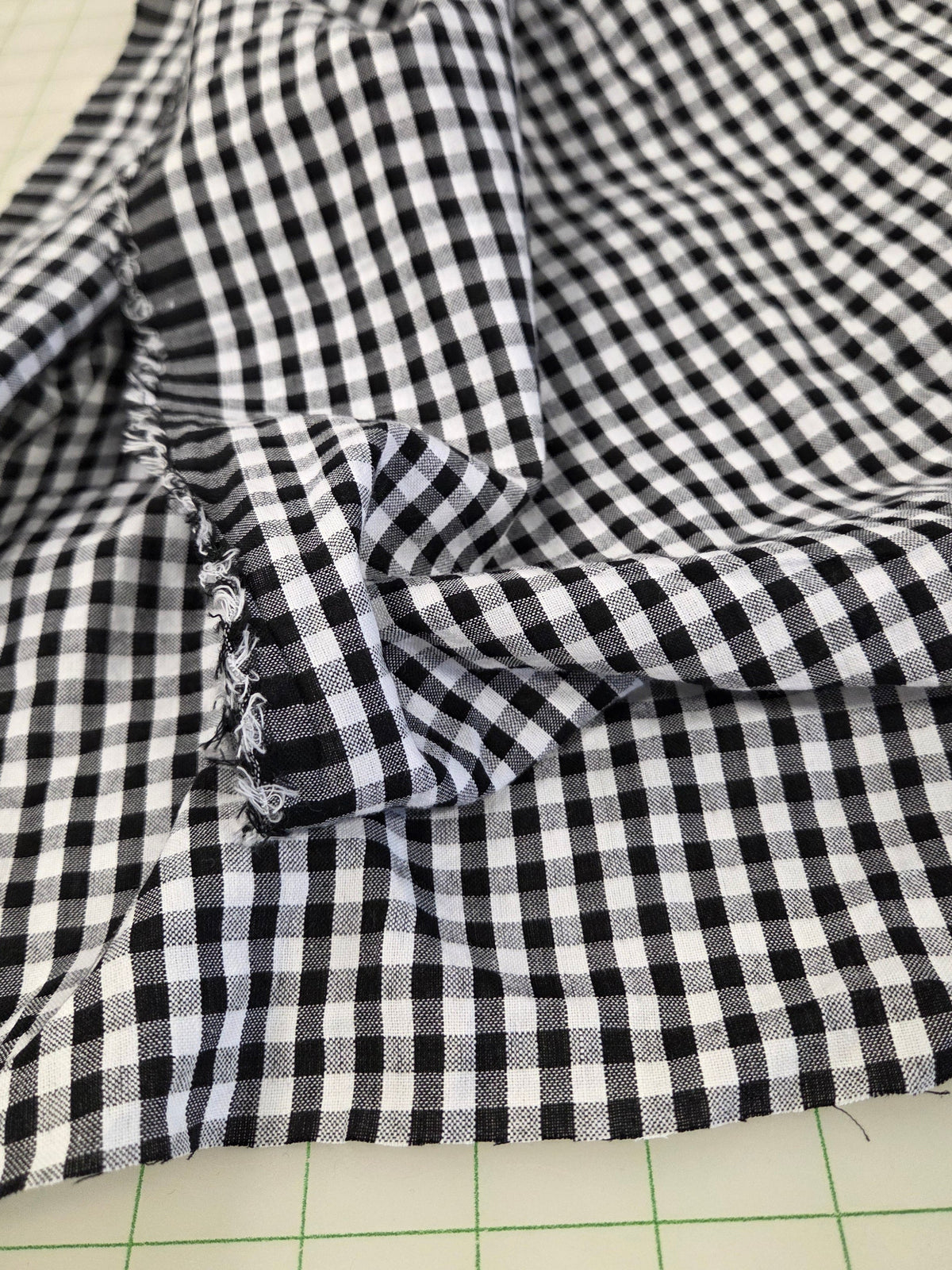 Black and white gingham checkered fabric draped over a green grid cutting mat.