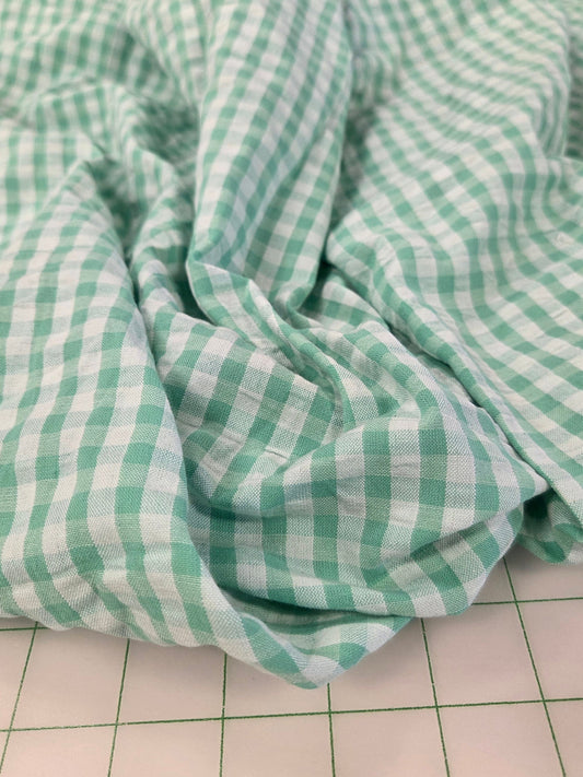 Green and white gingham checkered fabric draped on a white cutting mat with grid lines.
