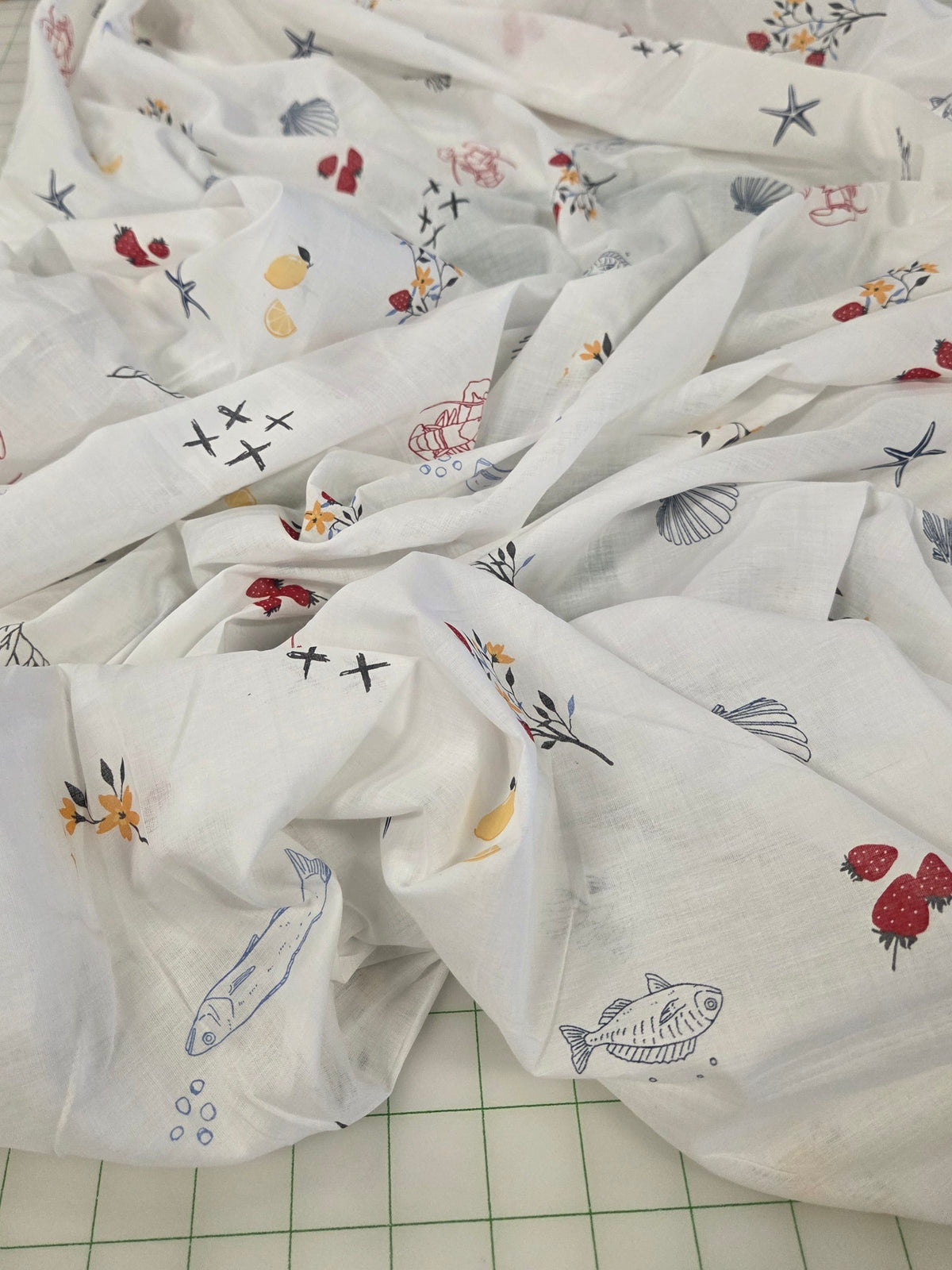 White muslin baby swaddle blanket with colorful nautical and floral prints, draped on a green grid cutting mat.
