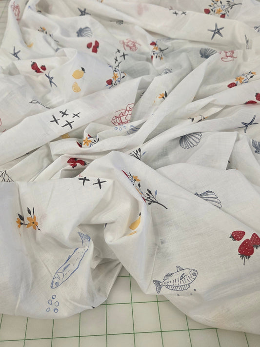 White muslin baby swaddle blanket with colorful nautical and floral prints, draped on a green grid cutting mat.