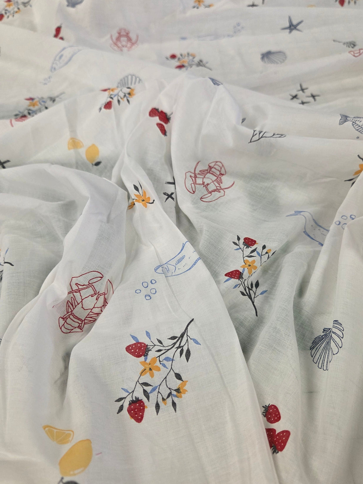 White sheer fabric with a colorful embroidered pattern of sea creatures, fish, and small flowers.