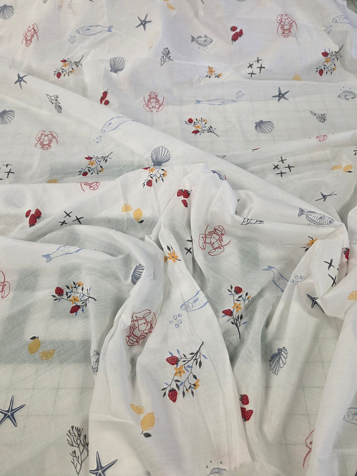 White sheer fabric printed with a colorful nautical and floral pattern, draped to show its texture and print.