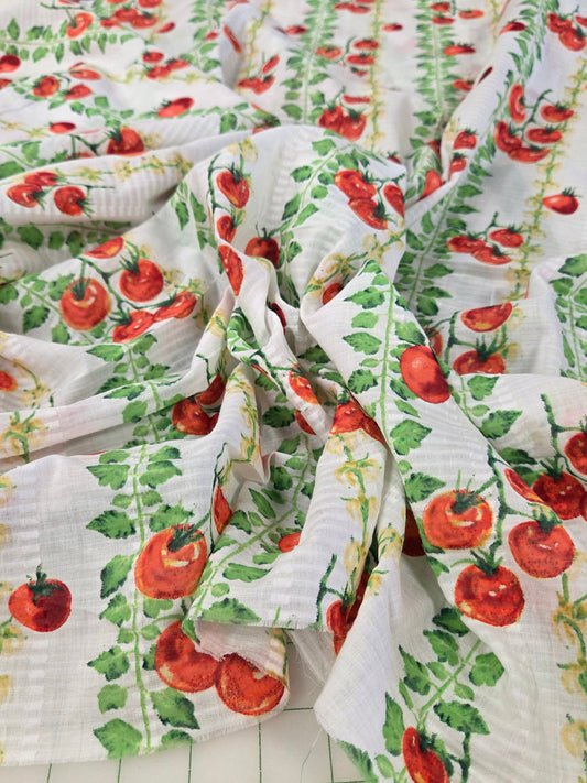 White muslin fabric printed with a red tomato and green vine pattern, draped to show its texture and print.