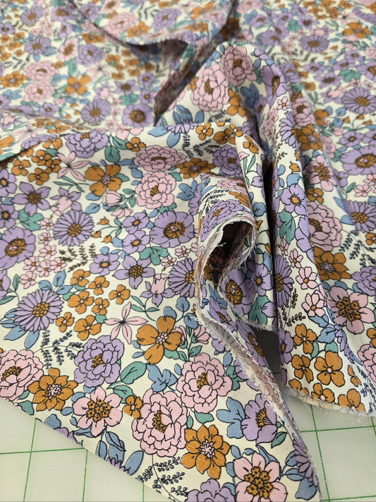 A close-up of a floral fabric with a vintage pattern of pink, purple, and orange flowers on a cream background, draped over a green cutting mat.