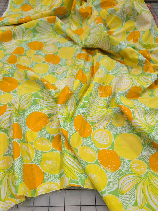 A piece of patterned fabric with a bright yellow and orange citrus fruit print on a light green background, laid out on a gridded cutting mat.