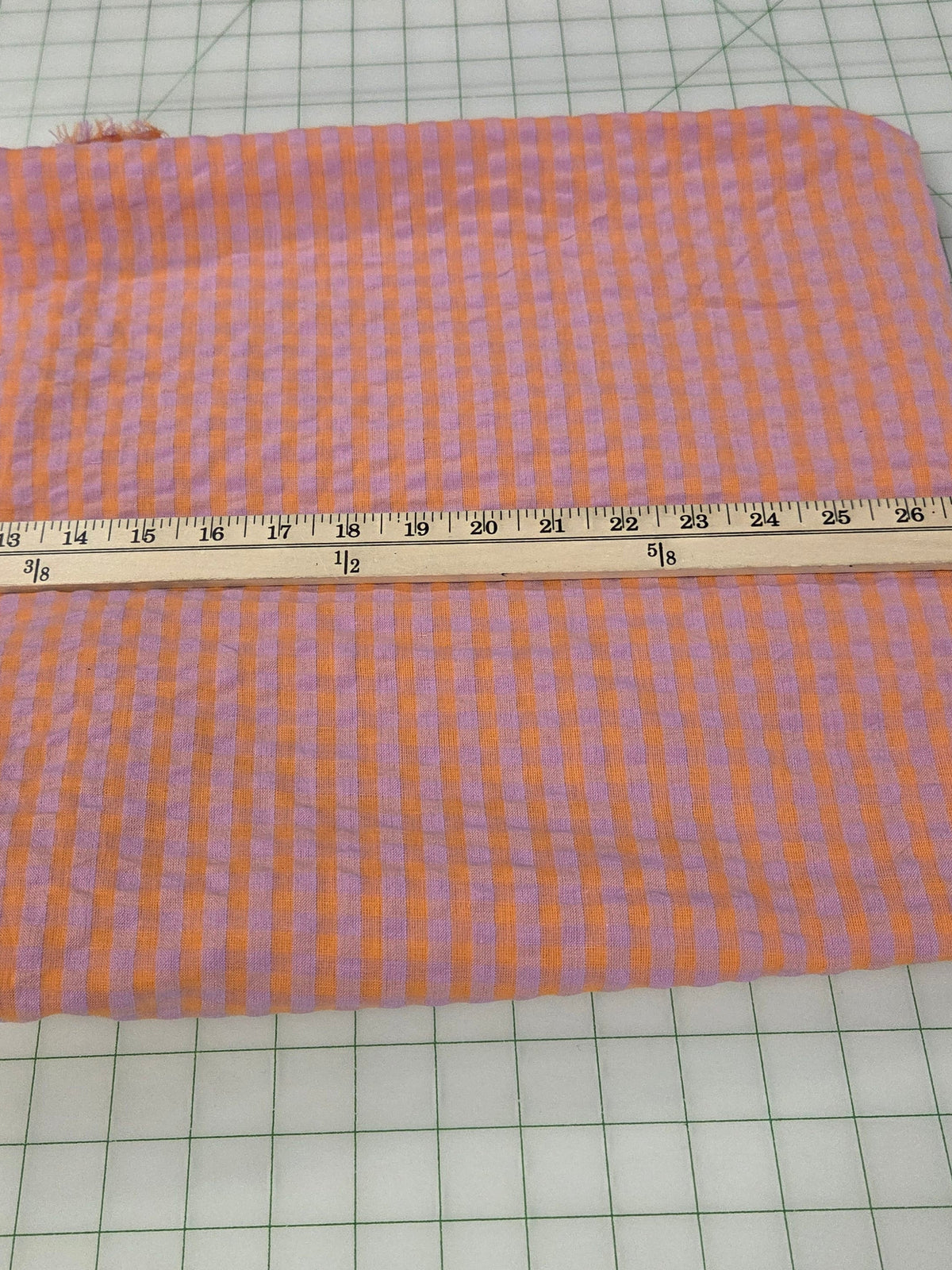 A piece of orange and purple gingham fabric laid flat on a white cutting mat with a wooden ruler measuring its width.
