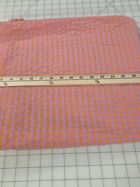 A piece of orange and purple gingham fabric laid flat on a white cutting mat with a wooden ruler measuring its width.